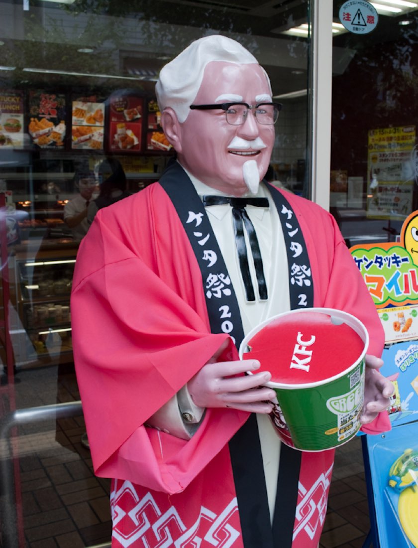 A Colonel Sanders statue dressed in a red Japanese happi coat, holding a KFC bucket.