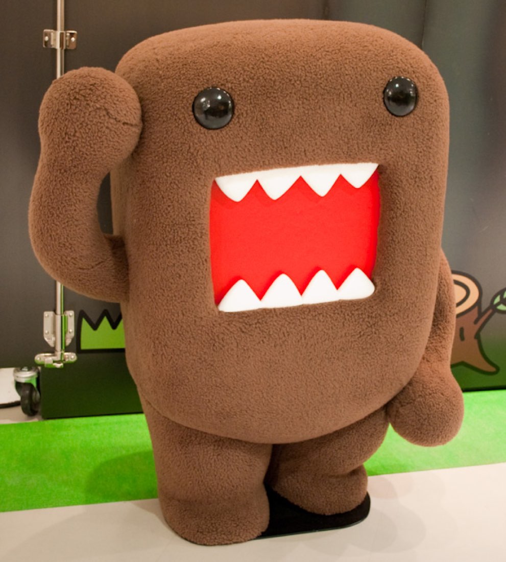 A full-body Domo-kun costume standing on green carpet, mouth fixed wide open.