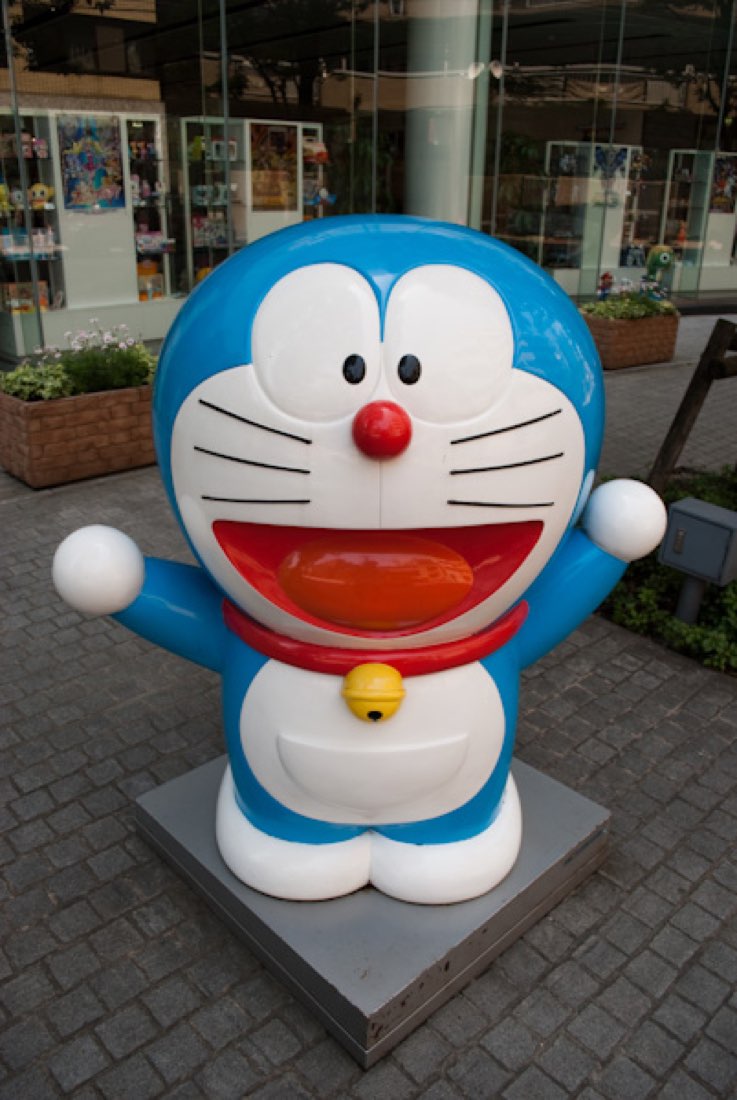 A Doraemon statue, blue and white robotic cat with a red nose and bell, arms raised.