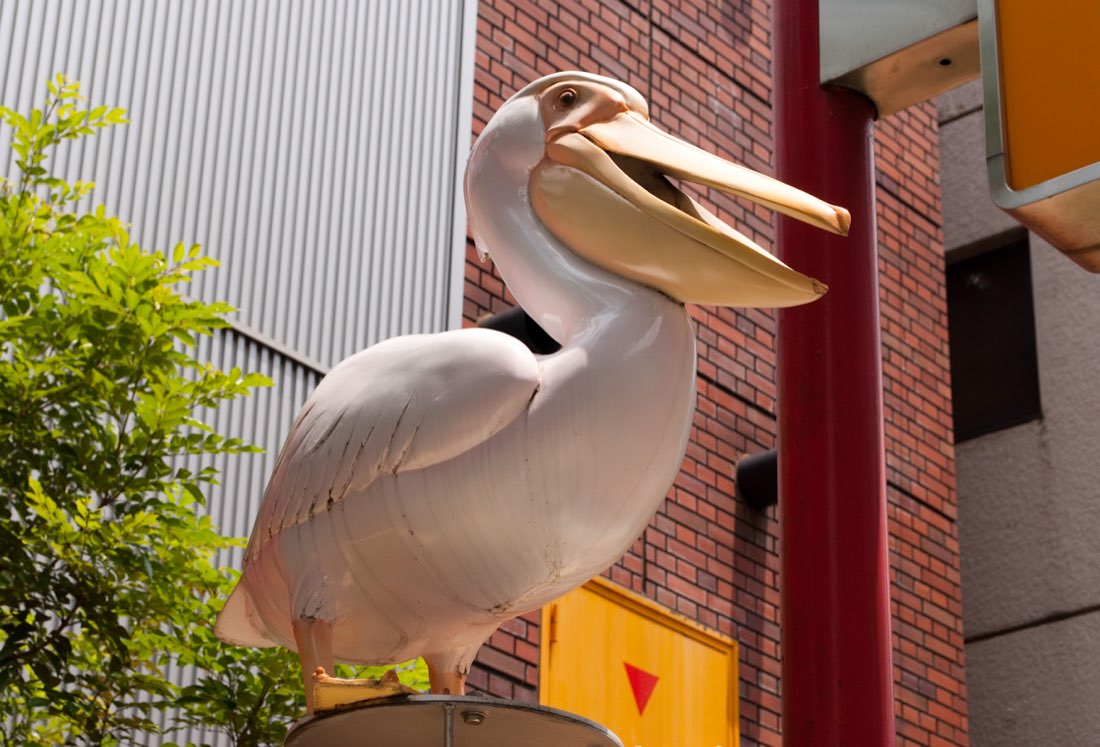 A large pelican statue perched on a brick building, beak in profile.
