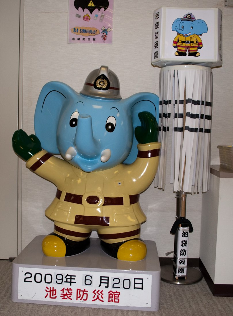 A blue elephant statue in a beige firefighter's uniform and helmet, one arm raised.