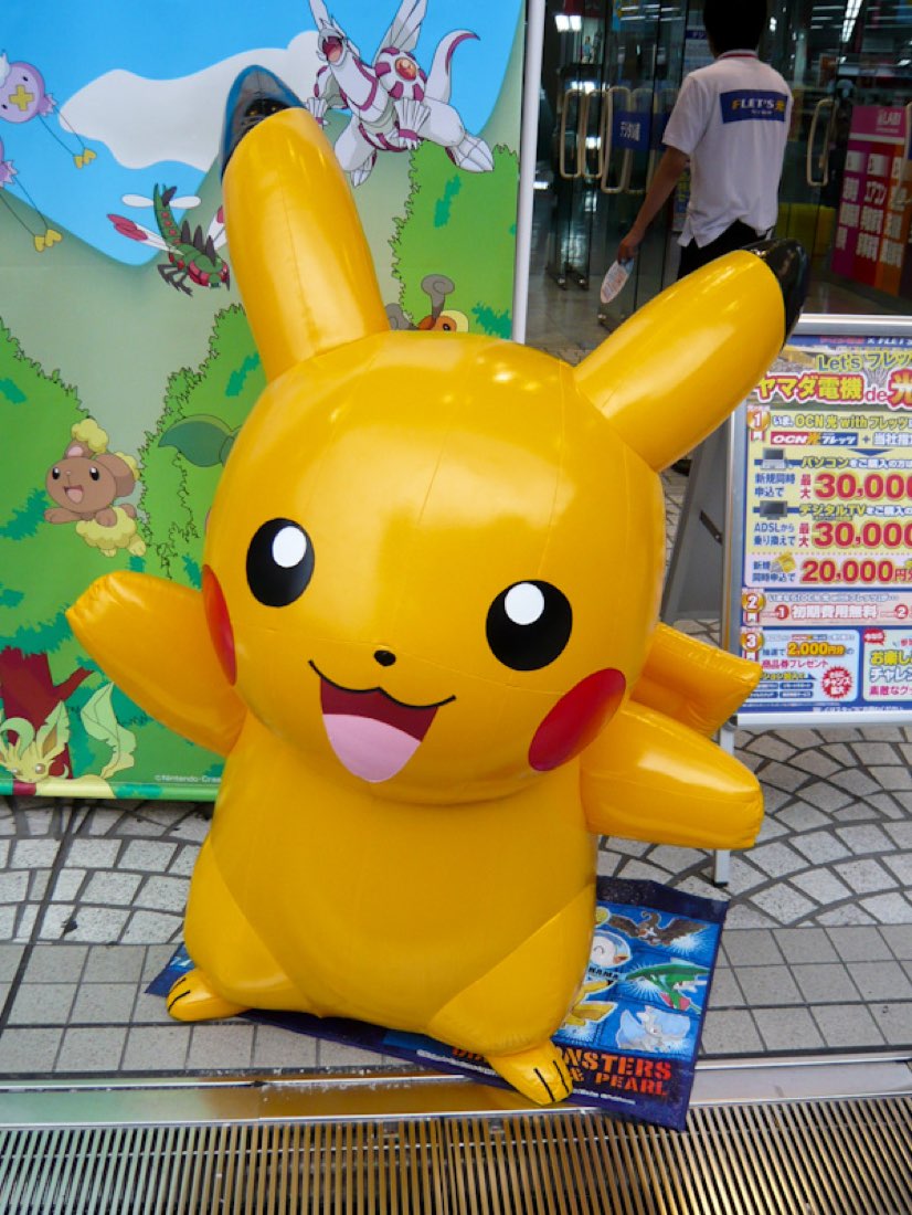 An inflatable Pikachu and an inflatable black-and-white Suica penguin outside an electronics shop.