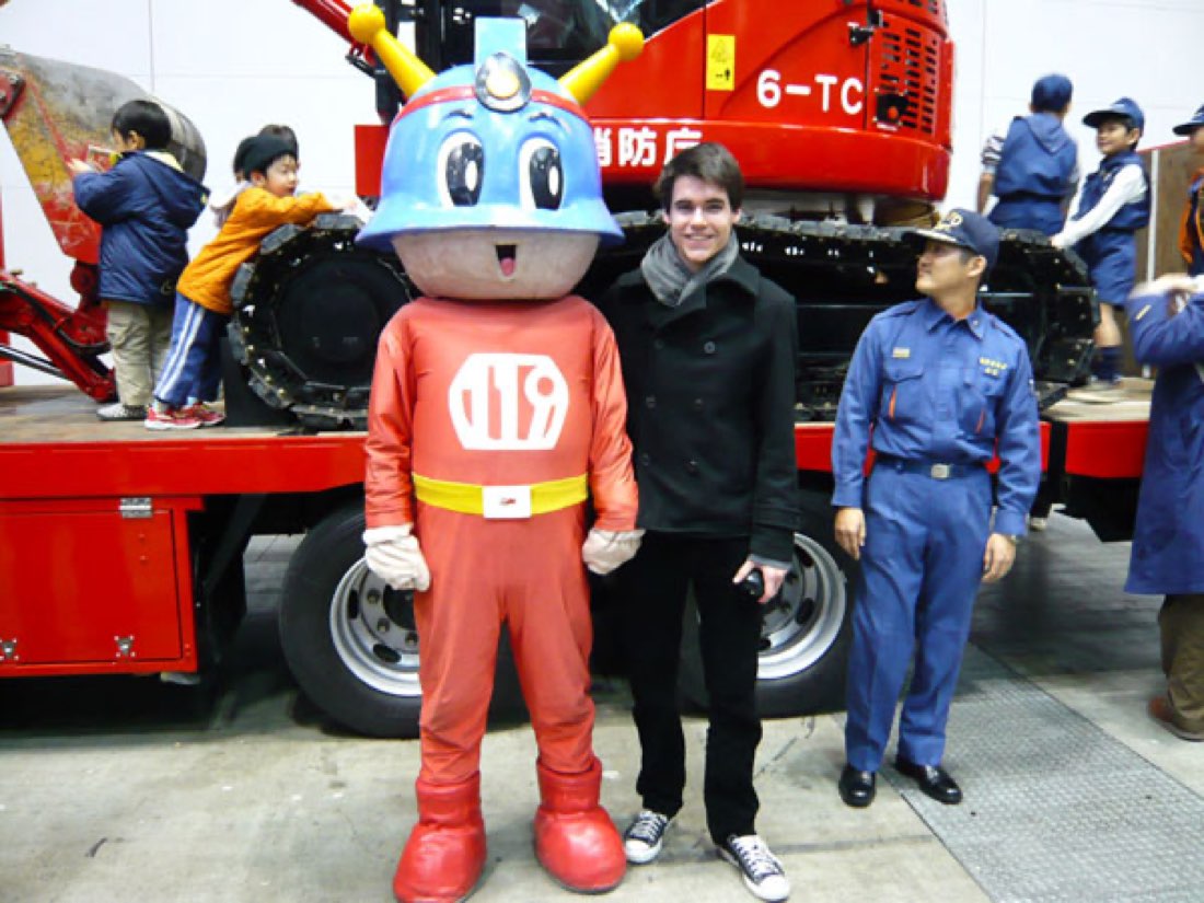 A person in a full-size Kyūta costume standing with firefighters in front of a fire engine.