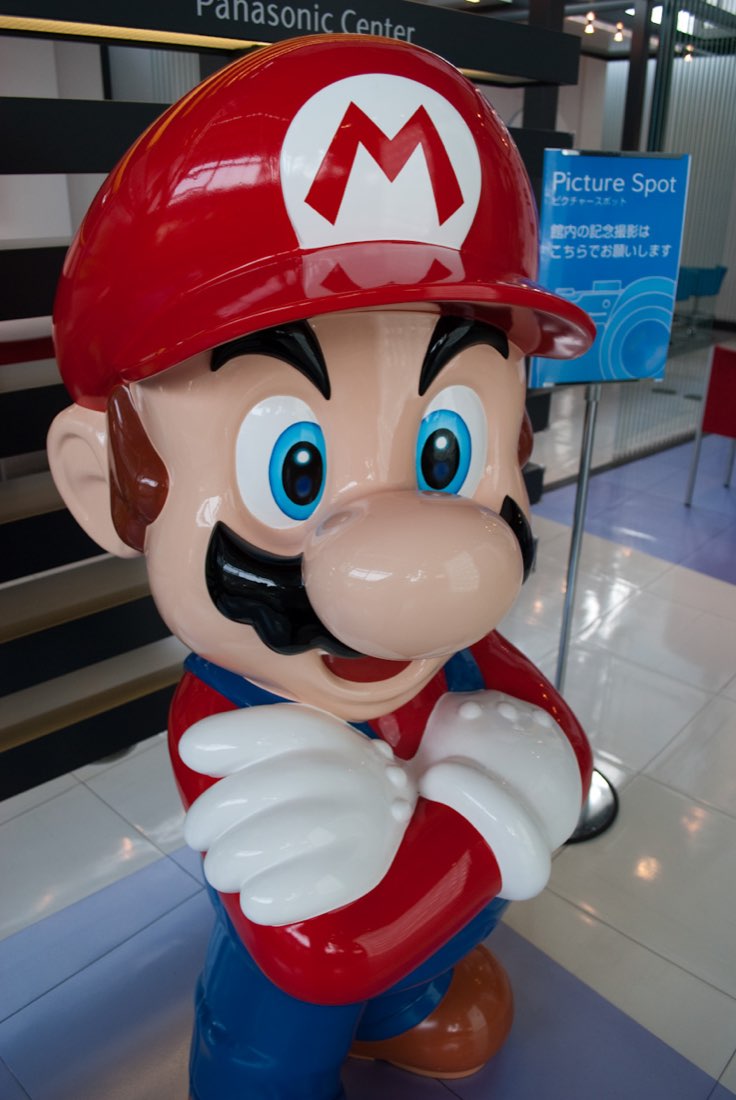 A Mario statue with arms folded inside a shop, beside a display of socks.