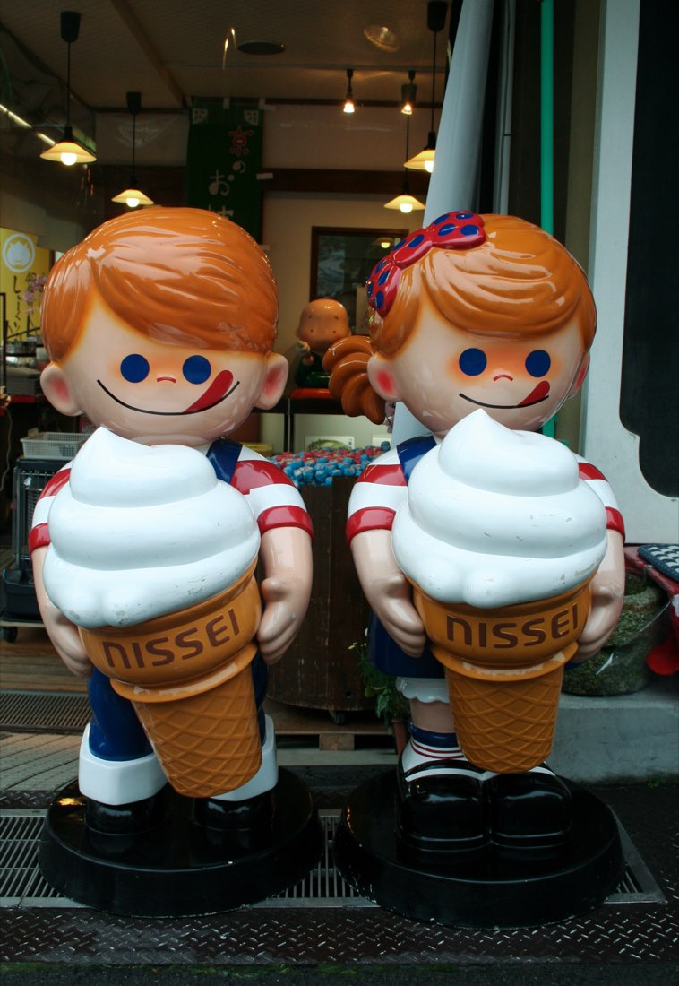 Twin mascots Ni-kun and Sei-chan, red-haired children each hugging a giant soft-serve ice cream cone.