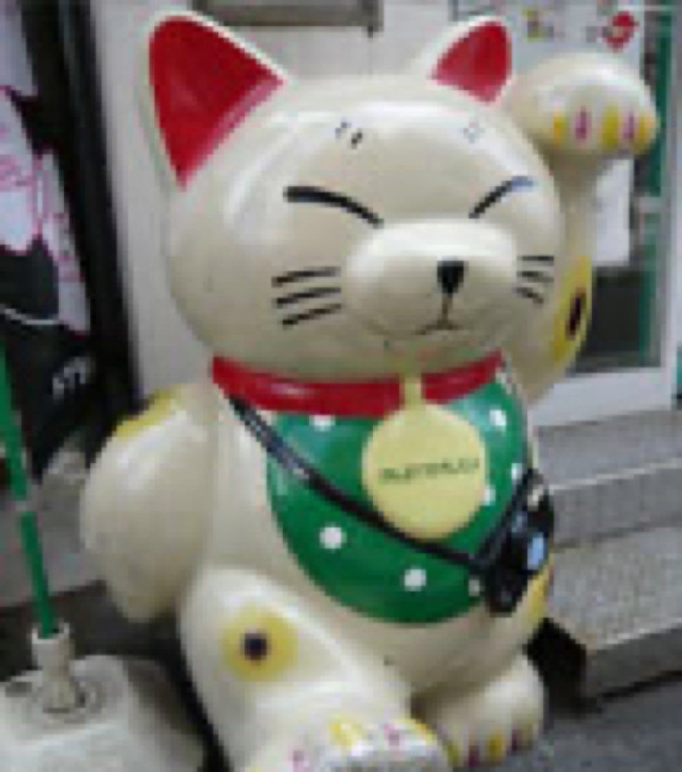 Nyanta, a beckoning-cat mascot with a green bib and a camera on a strap round his neck.