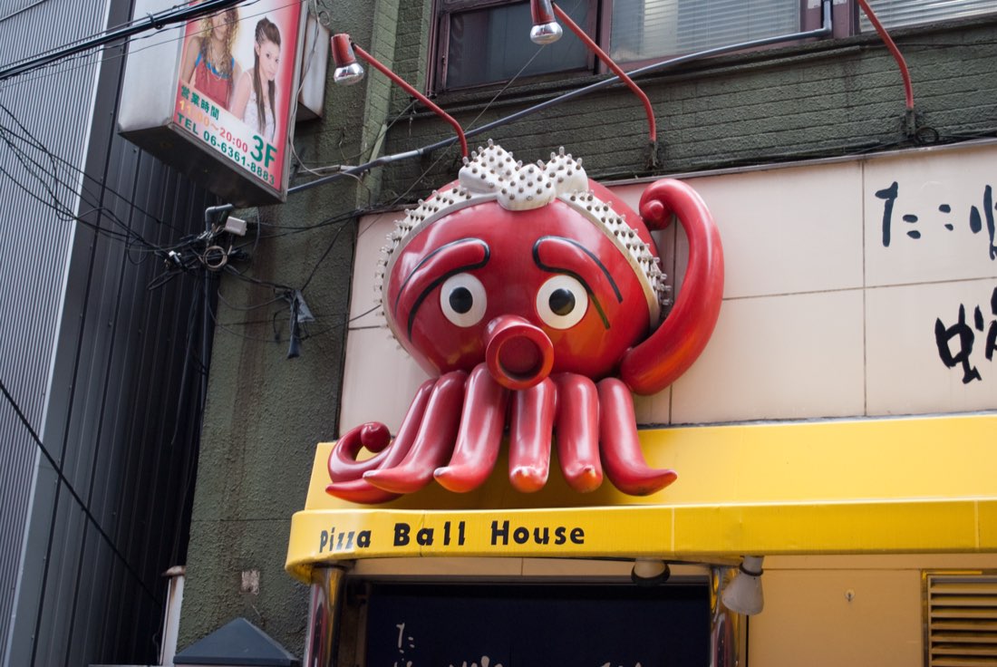 A red octopus statue in a white headscarf mounted above a shop sign reading Pizza Ball House.