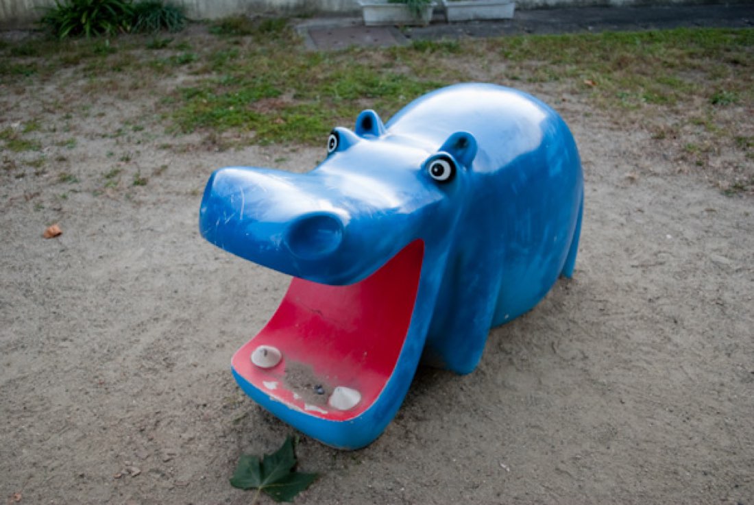 A blue playground hippo with its mouth wide open, set in sand.