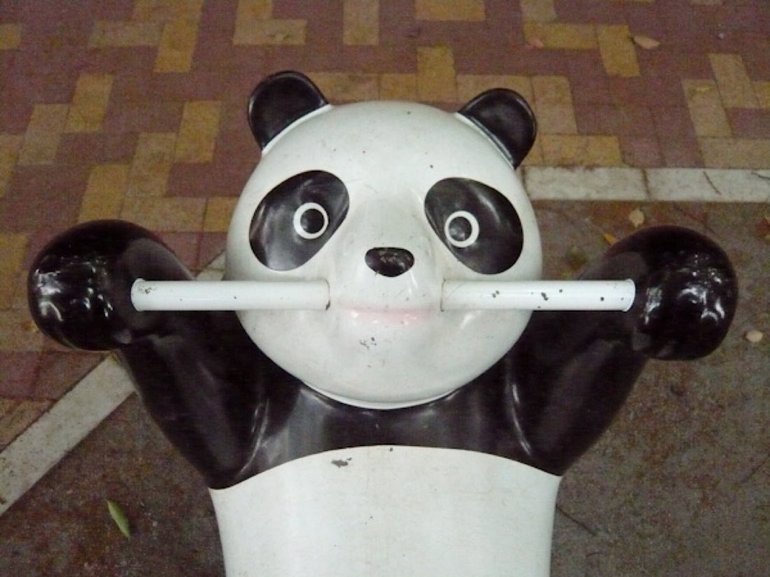 A worn playground panda with a metal pole through its mouth, paws raised.