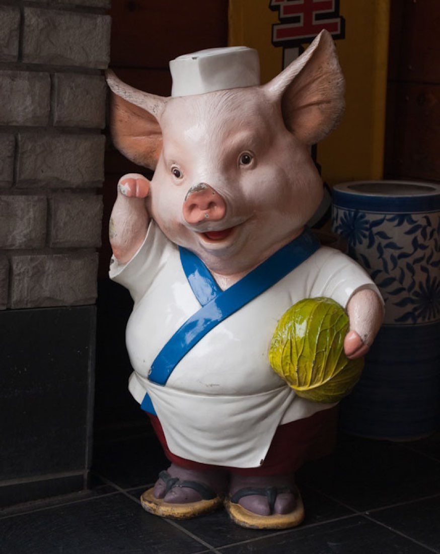 A pig statue in white chef's clothing and blue sash, cradling a gourd.