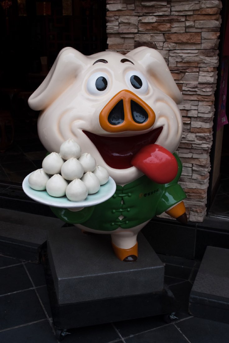 A pig statue holding a plate of white dumplings while licking its lips.