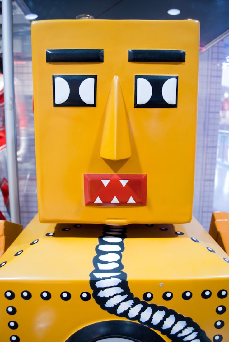 Close-up of a yellow robot's head with rectangular eyes and a jagged mouth.