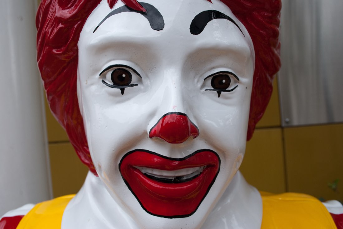 Close-up of a Ronald McDonald statue's face, white greasepaint and red smile.