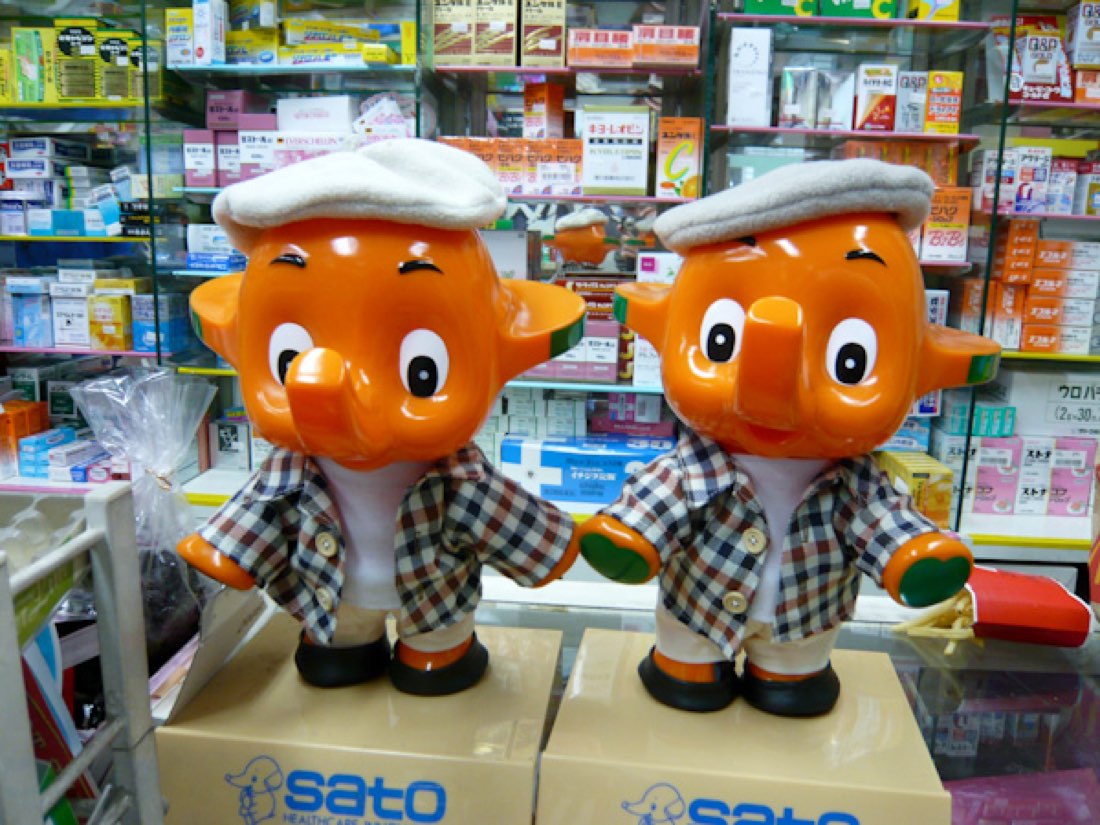 Two boxed Sato elephant mascots in flat caps and checked jackets, fresh from the factory.