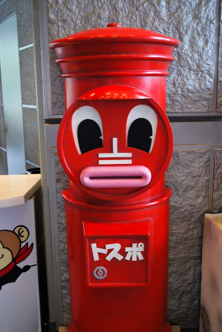 Tospo, a red postbox with a face: heavy-lidded eyes and a letter-slot mouth.