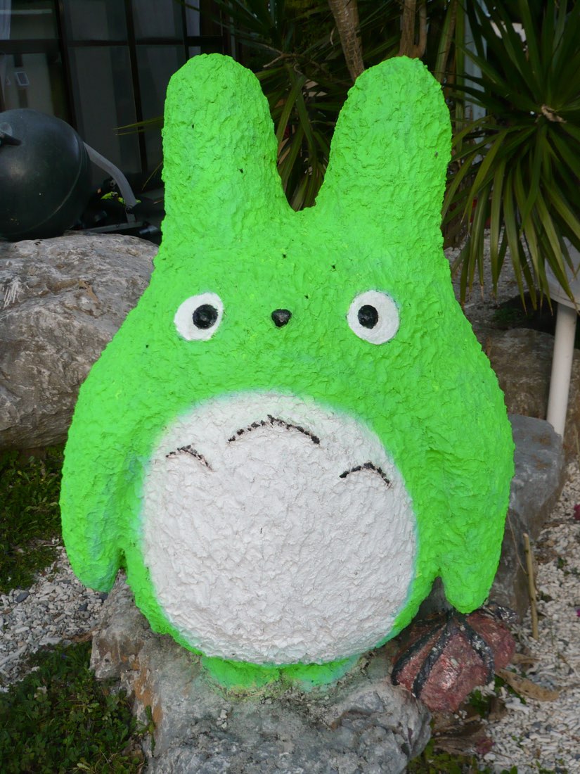A home-made bright green Totoro figure with wonky painted eyes, standing outdoors.