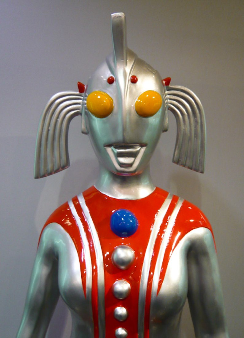 A silver-and-red Ultra hero statue with curled pigtail-like horns and orange eyes.