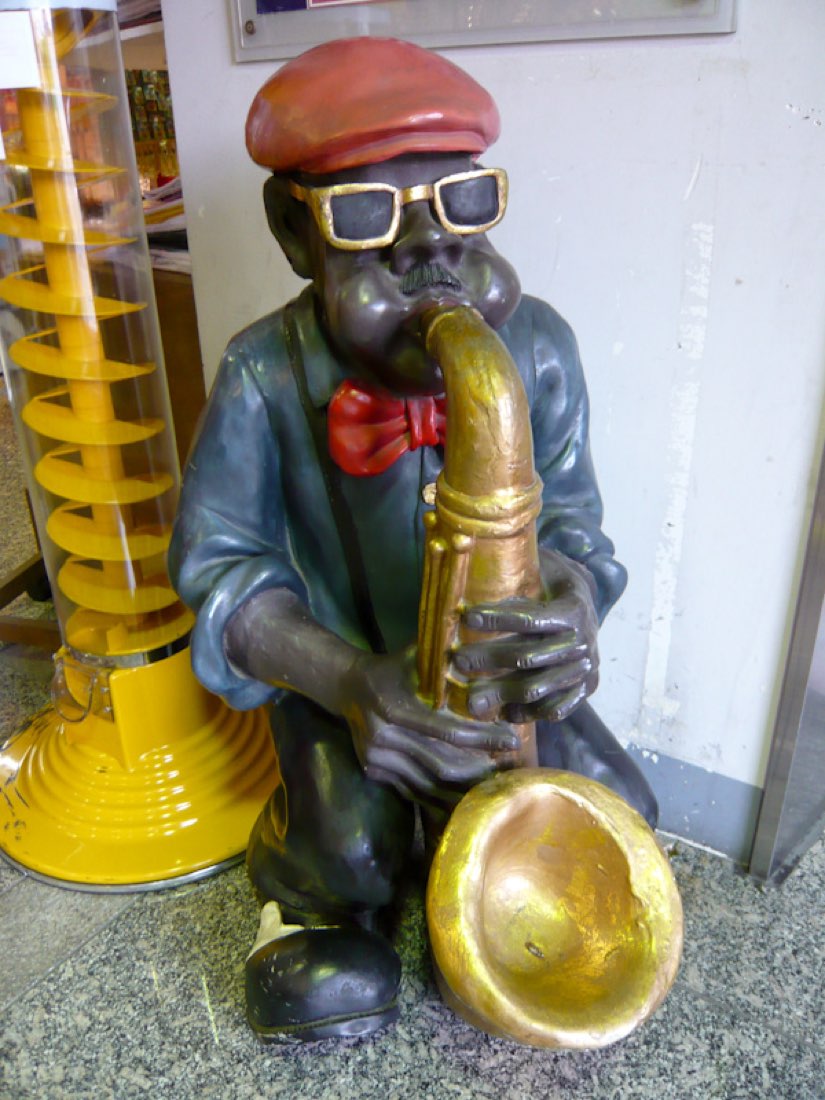 A carved wooden figure in sunglasses playing a golden saxophone.